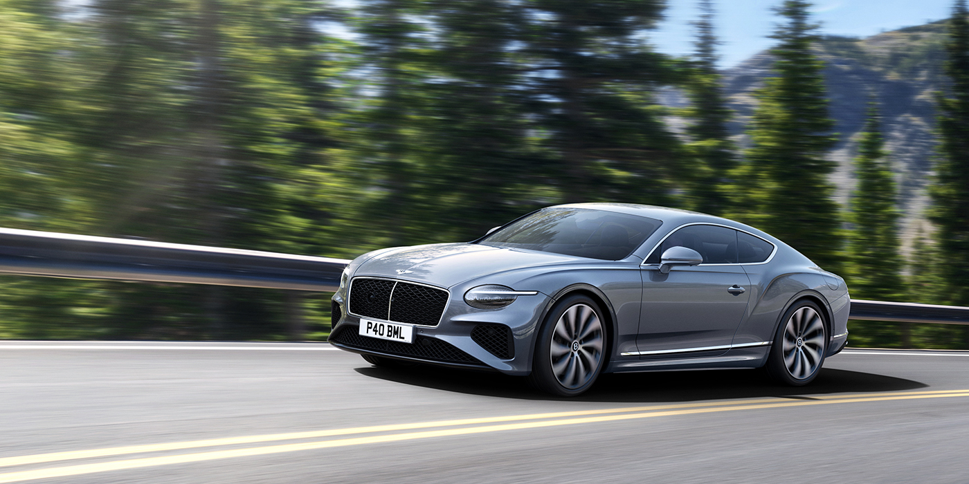 Bentley Taichung New Bentley Continental GT coupe in Silverlake paint and 22 inch ten-spoke wheels, driving dynamically on a tree-lined road in the sunshine