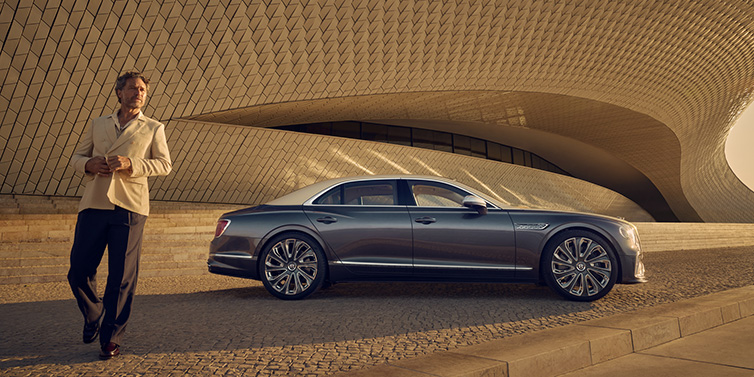 Bentley Taichung Bentley Flying Spur Mulliner sedan in Rose Gold over Magnetic duotone paint parked by a curved wall with person in suit jacket standing on the left